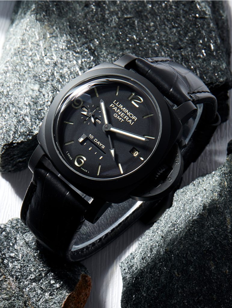 Panerai Luminor GMT watch with a black dial and leather strap, featuring a 10-day power reserve indicator, displayed on a textured rock background.